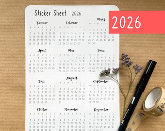 May include: White sticker sheet with calendar layouts for the year 2026. The months are written in German. A red rectangle with the number "2026" is in the upper right corner. A black pen and decorative tape are next to the sticker sheet.