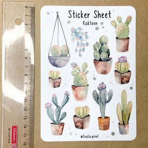 Może przedstawiać: Arkusz naklejek z akwarelowymi ilustracjami r&oacute;żnych kaktus&oacute;w w doniczkach. Arkusz zawiera tekst "Sticker Sheet Kakteen" i podpis artysty. Obok arkusza naklejek umieszczono linijkę.