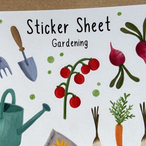 May include: Sticker sheet with a gardening theme. The sheet includes a watering can, a trowel, a fork, a tomato plant, two radishes, two carrots, and a seed packet. The sheet is white with green and brown dots.