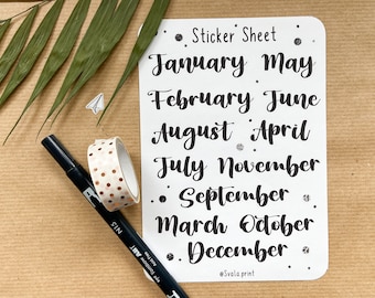 May include: A white sticker sheet with the months of the year written in black cursive script. The sheet is surrounded by small silver glitter dots. The text "Sticker Sheet" is at the top of the sheet. The text "@Svala print" is at the bottom of the sheet.