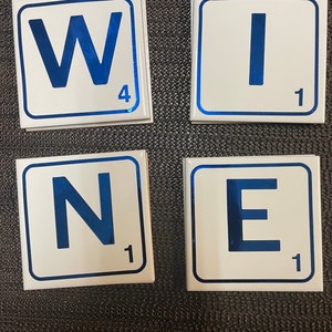 May include: Four white ceramic tiles with blue borders and blue letters spelling out the word "WINE". Each tile has a number on the bottom right corner.