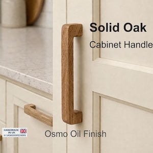 Puede incluir: Tiradores de armario de roble macizo con acabado al aceite Osmo. La imagen muestra un primer plano de un tirador de madera fijado a una puerta de armario color crema. El tirador es rectangular con bordes redondeados y veta de madera natural.