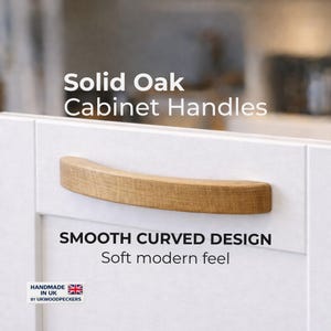 Puede incluir: Tirador de armario de roble macizo con un diseño curvo y suave. El tirador es de color marrón claro y está montado en una puerta de armario blanca. El texto "Solid Oak Cabinet Handles" y "Smooth Curved Design" es visible.