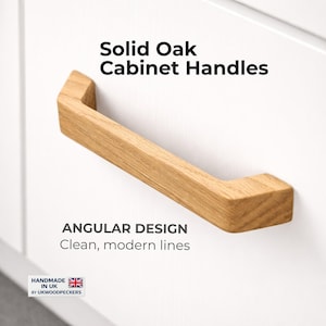 Könnte beinhalten: Massive Eichenholz-Schrankgriff mit kantigem Design. Der Griff ist aus hellbraunem Holz gefertigt und an einer weißen Oberfläche befestigt. Der Text "Solid Oak Cabinet Handles" und "Angular Design" ist sichtbar.