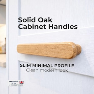 Puede incluir: Tirador de armario de roble macizo con un perfil delgado y minimalista. El tirador es de color marrón claro y está montado en una puerta de armario blanca. El texto dice "Solid Oak Cabinet Handles" y "SLIM MINIMAL PROFILE Clean modern look".