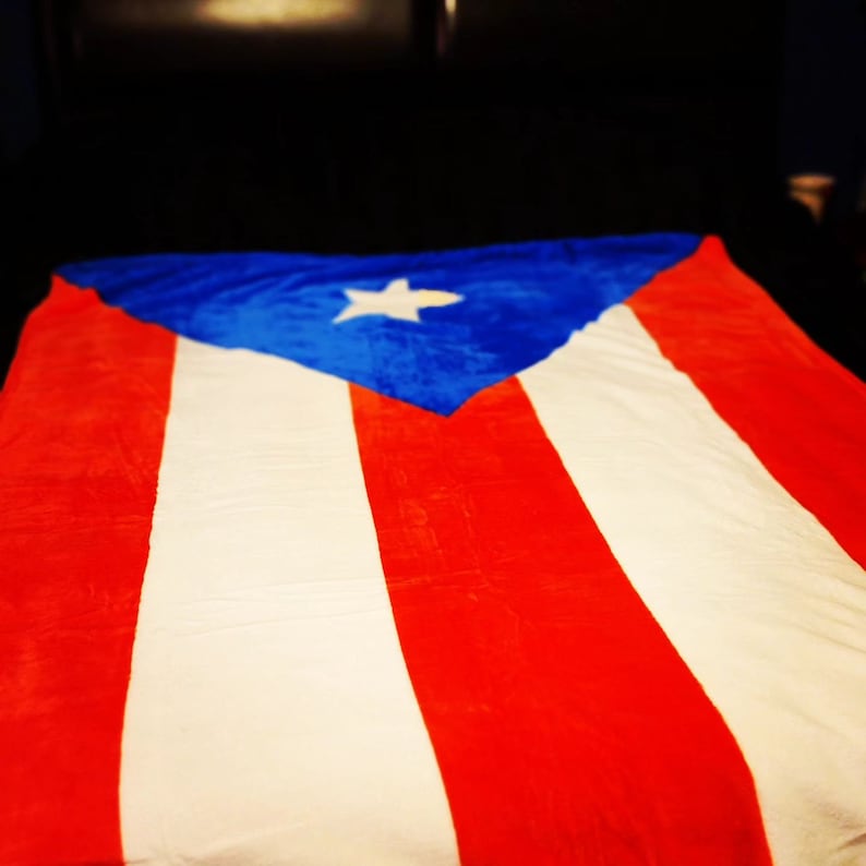 May include: A red, white and blue blanket with a white star on a blue triangle in the centre. The blanket is made of soft, plush fabric.