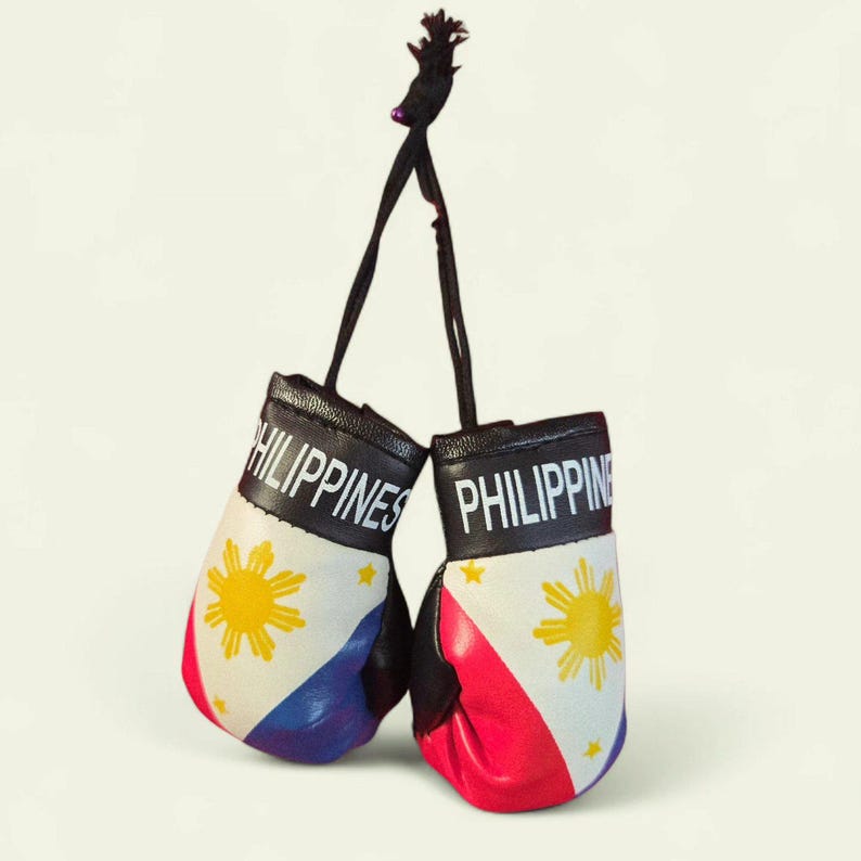 Puede incluir: Mini guantes de boxeo con la palabra "PHILIPPINES" en letras blancas. Los guantes presentan la bandera de Filipinas: un tri&aacute;ngulo blanco, un sol con ocho rayos y campos azules y rojos. Cuelgan correas negras de los guantes.