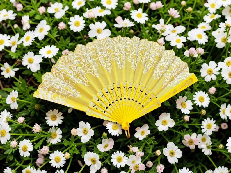 May include: A bright yellow folding hand fan featuring an intricate white lace pattern along the top edge and a solid yellow plastic frame with decorative cutouts at the base, displayed in a fully open, semi-circular position.
