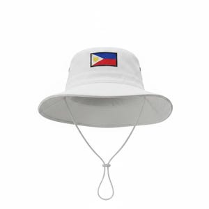 May include: White bucket hat featuring the flag of the Philippines. The hat has a wide brim and a chin strap with an adjustable toggle. The flag is embroidered on the front of the hat. This hat is a stylish accessory for sun protection.