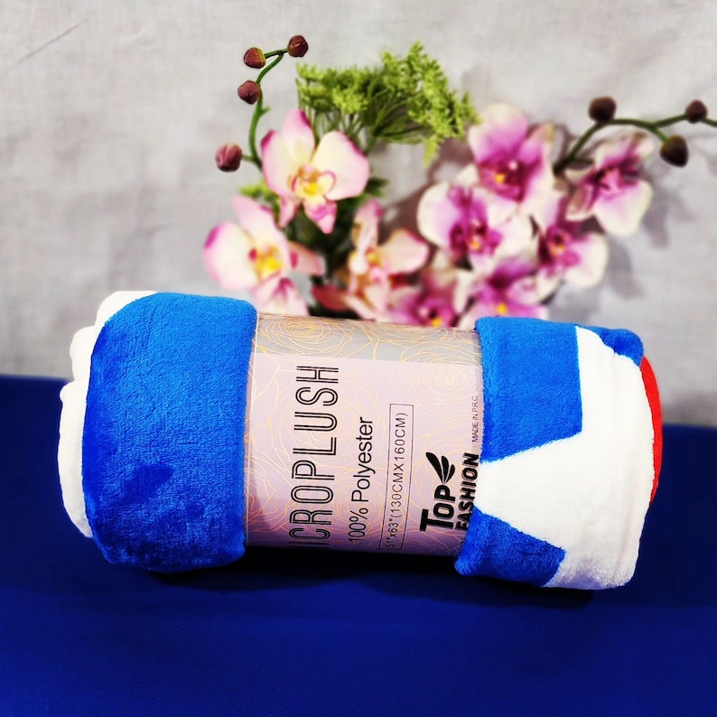 May include: A rolled up blue, white and red blanket with a label that reads "Microplush 100% Polyester 1130CMx160CM" and "Top Fashion" with a leaf logo.