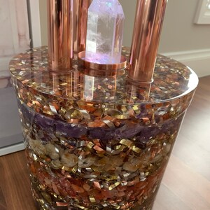 Puede incluir: Un orbe de vidrio transparente lleno de capas de cristales de diferentes colores y tuber&iacute;as de cobre. El orbe contiene varios cristales, incluyendo amatista, citrino y cuarzo rosa. Las tuber&iacute;as de cobre est&aacute;n dispuestas en forma triangular alrededor del orbe.