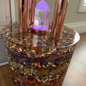 Puede incluir: Un punto de cristal transparente se asienta sobre un soporte de cobre con una base de resina y incrustada con varios cristales y escamas met&aacute;licas. La base est&aacute; compuesta por diferentes colores, incluyendo morado, marr&oacute;n, dorado y cobre.