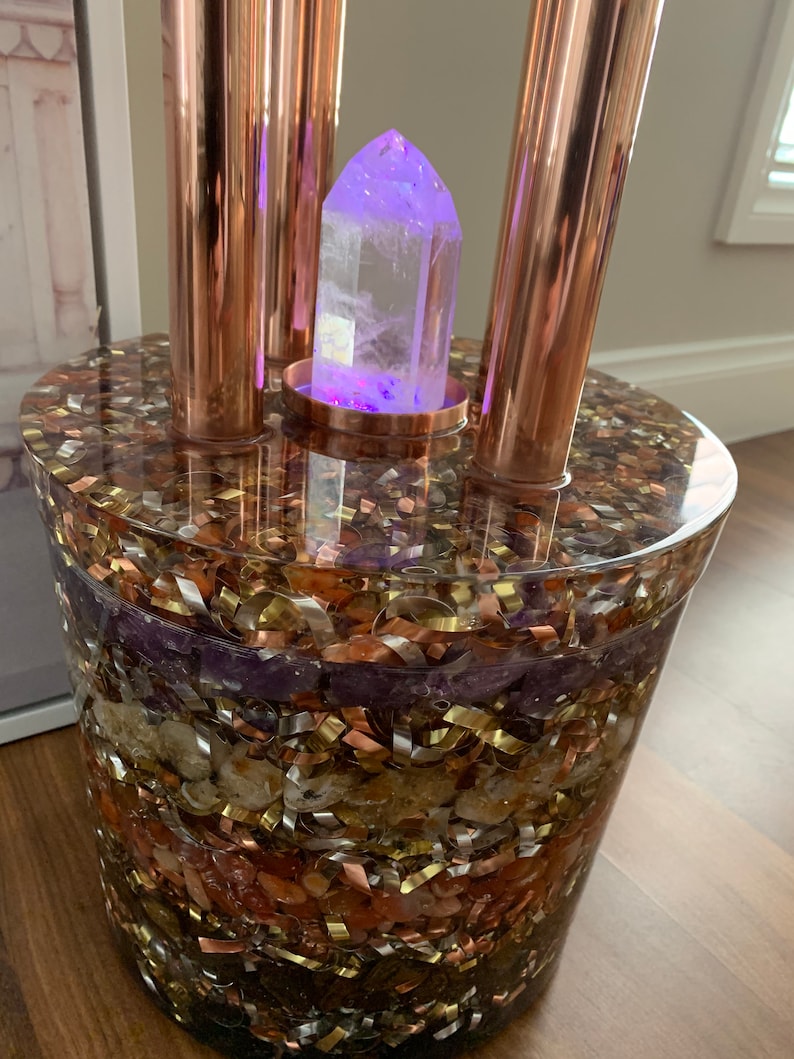 Puede incluir: Un punto de cristal transparente se asienta sobre un soporte de cobre con una base de resina y incrustada con varios cristales y escamas met&aacute;licas. La base est&aacute; compuesta por diferentes colores, incluyendo morado, marr&oacute;n, dorado y cobre.
