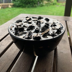Puede incluir: Un cuenco negro lleno de trozos de carbón vegetal negro. El cuenco está sobre una mesa de madera.