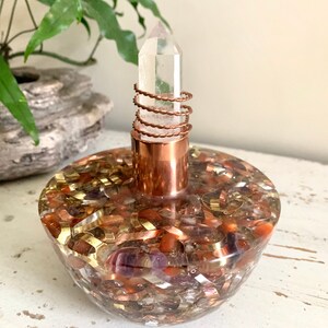 Puede incluir: Un punto de cristal de cuarzo claro se asienta sobre una base envuelta en alambre de cobre. La base está llena de una resina transparente que contiene varios cristales, incluyendo amatista, cornalina y cobre.