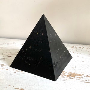 Puede incluir: Objeto negro en forma de pirámide con una superficie moteada y brillante. La pirámide está hecha de resina y tiene un acabado liso y pulido.