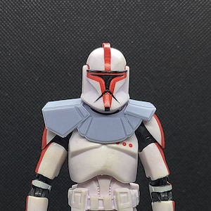 May include: A white and red action figure of a Star Wars clone trooper with a blue chest plate and a black visor.