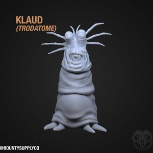 Könnte beinhalten: Ein 3D-gedrucktes Modell einer grauen außerirdischen Kreatur mit einem großen Kopf, zwei Augen und einem Mund. Die Kreatur hat sechs lange, dünne Gliedmaßen, die sich von ihrem Kopf erstrecken. Das Modell ist mit "KLAUD (TRODATOME)" beschriftet.