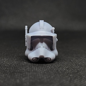 May include: A white plastic clone trooper helmet with a black visor and a gray antenna. The helmet is designed to look like a Star Wars clone trooper helmet.
