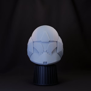 May include: A white plastic helmet with a grey visor and a black base. The helmet has a geometric design and is reminiscent of a futuristic soldier's helmet.