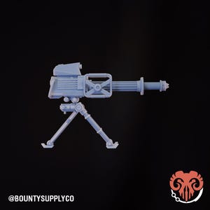 Puede incluir: Una ametralladora en miniatura de color azul claro con una base de trípode. El arma tiene una mira, un asa y un cañón. El texto "@BOUNTYSUPPLYCO" está en la parte inferior izquierda. La imagen está sobre un fondo negro.