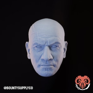 May include: A light blue, sculpted bust of a man's head with detailed facial features and markings. The head is bald and has a stern expression. The text "@BOUNTYSUPPLYCO" is at the bottom left.