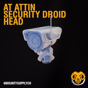 May include: A light blue security droid head with a camera lens and antenna, set against a black background. The text "AT ATTIN SECURITY DROID HEAD" is in yellow. The @BOUNTYSUPPLYCO logo is at the bottom.