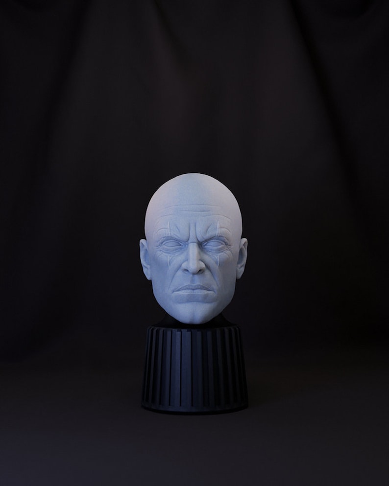 May include: A white bust sculpture of a bald man with a serious expression. The sculpture is on a black pedestal with a fluted design.