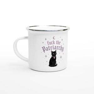 Könnte beinhalten: Weißer Emaillebecher mit silbernem Rand und Griff. Der Becher zeigt den Text "fuck the Patriarchy" in einer stilisierten Schriftart, zusammen mit einer schwarzen Katze mit herzförmigem Halsband. Sterne und ein Halbmond sind ebenfalls enthalten.
