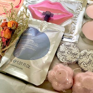 May include: A gift box filled with beauty products. Includes a bouquet of dried flowers, shampoo sachet, lip mask, two pink candles, two wrapped Elizabeth Shaw chocolates, and two pink flower-shaped bath bombs.