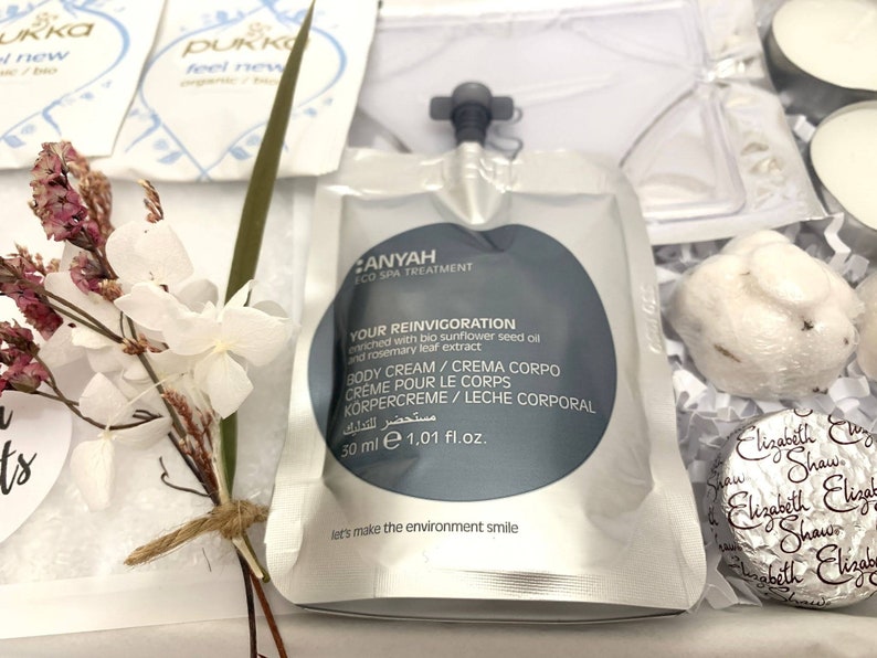 May include: A gift set featuring a white pouch of body cream, a small bouquet of dried flowers, and other spa products. The body cream is labeled "ANYAH ECO SPA TREATMENT" and "YOUR REINVIGORATION". The set includes a 50 ml pouch of body cream.