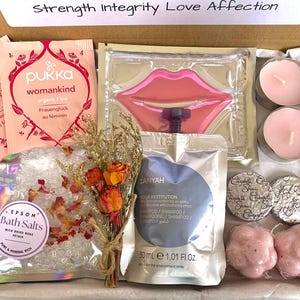 May include: A gift box filled with self-care items. Includes Pukka tea packets, a lip-shaped face mask, bath salts with rose petals, a small bouquet of dried flowers, shampoo, two candles, two bath sponges, and two wrapped soaps.