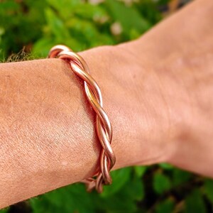 Könnte beinhalten: Ein Kupferarmband mit einem gedrehten Design. Das Armband wird am Handgelenk getragen.