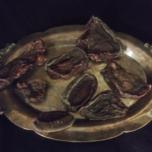 Puede incluir: Una bandeja de servir plateada con ocho trozos de fruta seca encima. La fruta es de color marrón oscuro y tiene una textura arrugada.