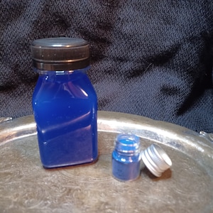 Pode incluir: Duas garrafas de líquido azul, uma maior e outra menor, em uma bandeja de prata. A garrafa maior tem uma tampa preta e a menor uma tampa prateada.