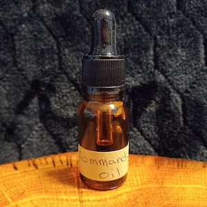May include: A small amber glass bottle with a black dropper top and a label that reads "Command Oil". The bottle is sitting on a wooden surface.