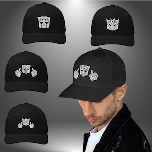 May include: Five black trucker hats with a white embroidered image of the Transformers logo.  The logo on four of the hats is the Autobot symbol, and the logo on one hat is the Decepticon symbol.  The hats have a mesh back.