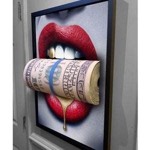 Pode incluir: Um close-up de uma pintura que retrata um par de lábios vermelhos com dentes de ouro mordendo um rolo de notas de dólar americano. As notas são envoltas com uma faixa azul e os dentes de ouro pingam tinta dourada.