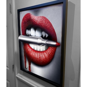 May include: A framed canvas print of a close-up of a woman's red lips with fangs biting down on a silver bullet. Blood drips from the corners of the mouth.