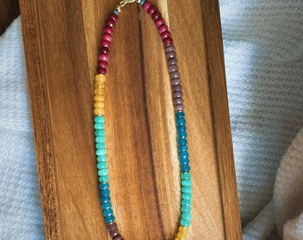 May include: A multi-colored beaded necklace with a gold clasp. The beads are red, orange, yellow, green, blue, and purple.