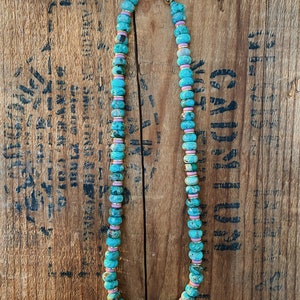 May include: A turquoise and pink beaded necklace with a gold clasp. The beads are round and have a speckled pattern.