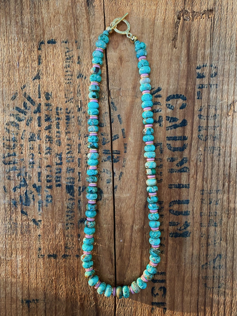 May include: A turquoise and pink beaded necklace with a gold clasp. The beads are round and have a speckled pattern.