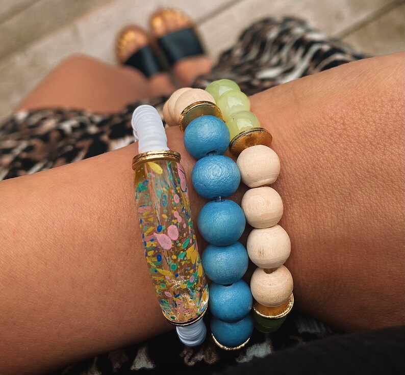 Puede incluir: Un conjunto de tres pulseras con cuentas de colores. La pulsera superior es blanca con una cuenta tubular transparente con motas de colores. La pulsera del medio est&aacute; hecha de cuentas de color azul claro y crema. La pulsera inferior est&aacute; hecha de cuentas de color verde claro y crema.