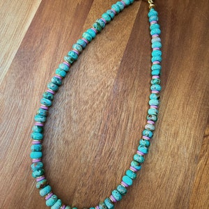 May include: A turquoise and pink beaded necklace with a gold clasp. The beads are round and have a marbled pattern.