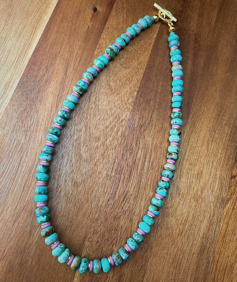 May include: A turquoise and pink beaded necklace with a gold clasp. The beads are round and have a marbled pattern.
