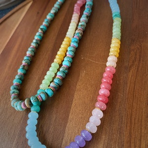 May include: Two layered necklaces with colorful gemstone beads. The top layer is turquoise, yellow, green, and pink. The bottom layer is light blue, purple, and pink.