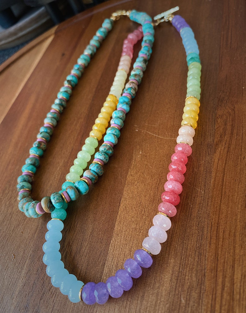 May include: Two layered necklaces with colorful gemstone beads. The top layer is turquoise, yellow, green, and pink. The bottom layer is light blue, purple, and pink.