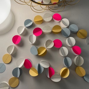 May include: A paper garland with alternating circles of grey, yellow, and pink. The circles are folded in half and strung together with a thin white string.