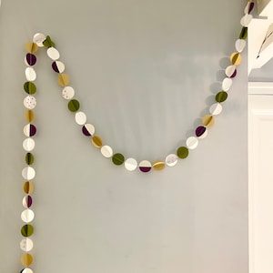 May include: A garland of paper circles in shades of green, gold, and purple. The circles are strung together with white thread and have a polka dot pattern.