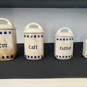 Può includere: Quattro barattoli in ceramica con bordi blu e bianchi. I barattoli sono etichettati "Sucre", "Cafe", "Farine" e "Epices".